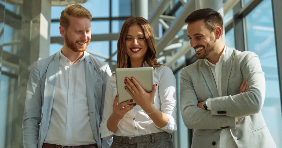 Three colleagues smiling while looking at a tablet